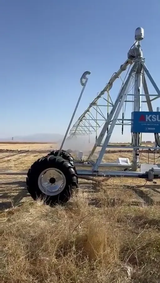 A drive tower wheel and span of an AksuPivot machine, with spray drifting past